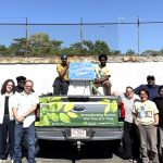Team standing in front of the watering truck with a poster announcing a Cummings Grant